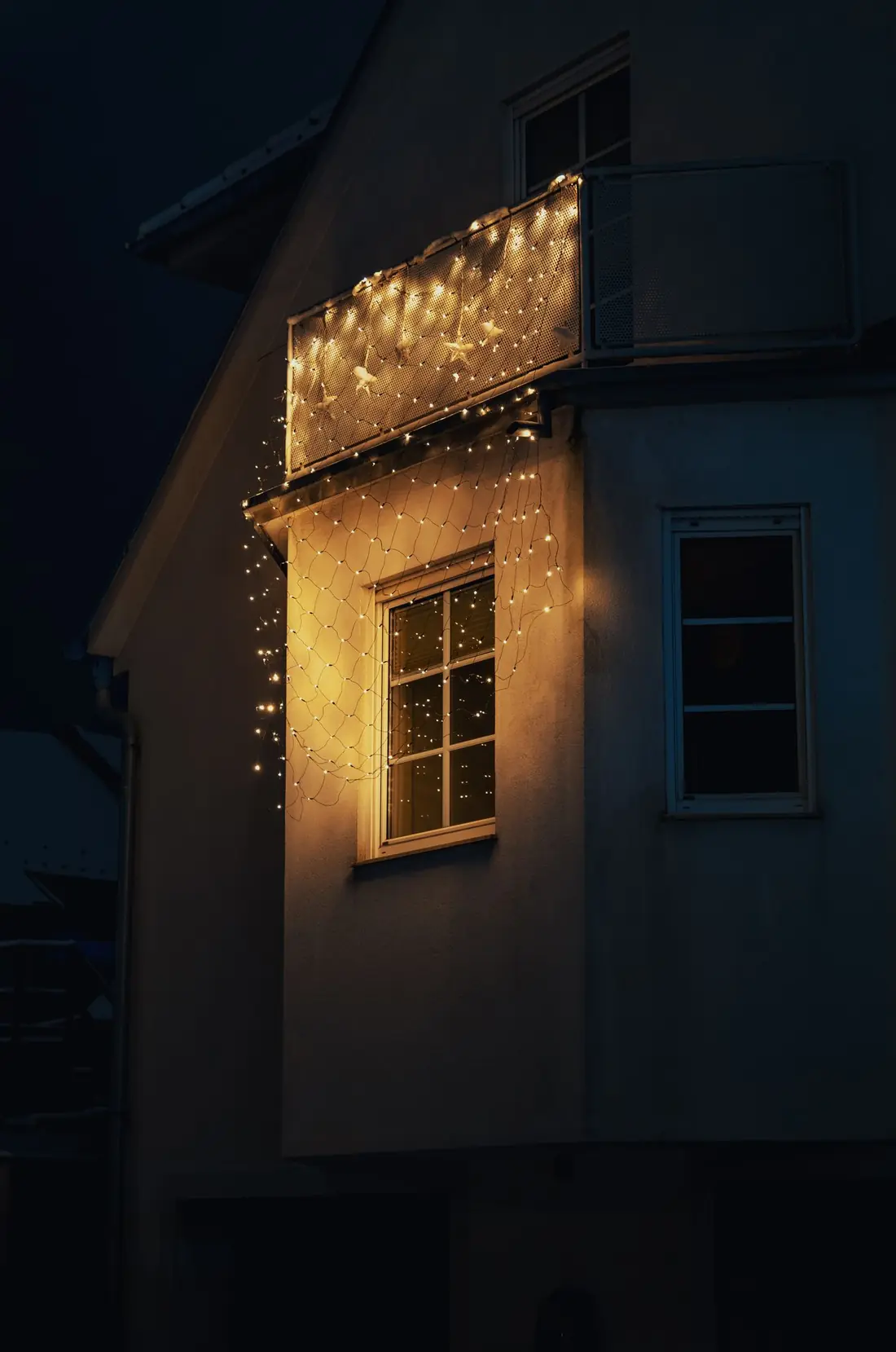 House at night with warm white lights along the balcony and roofline
