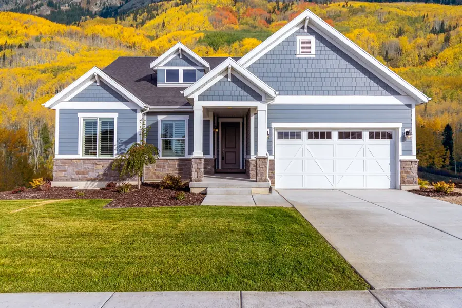 Freshly mowed green lawn in front of a gray house with golden trees behind